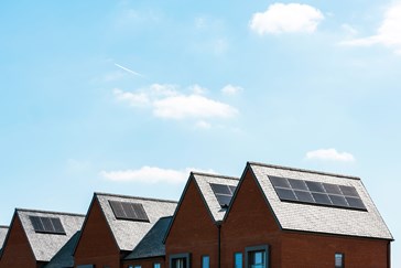 Row of modern brick houses with solar panels installed on grey pitched roofs